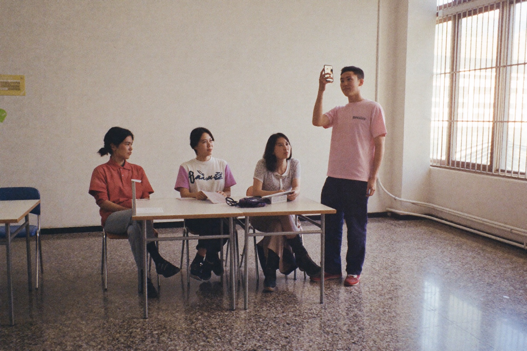 四位學員圍著桌子,其中一人直式握手機拍攝桌上的物件